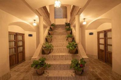 یک راه پله با گلدان‌های سبز در یک فضای داخلی با دیوارهای خمیده و درهای چوبی در عمارت محمودیه کاشان.