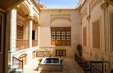 حیاط بنای تاریخی هتل فاضلی یزد با حوض آبی و پنجره های چوبی