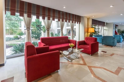 لابی هتل هما 2 مشهد با مبل های نشیمن قرمز و آبی و پنجره های رو به فضای سبز هتل