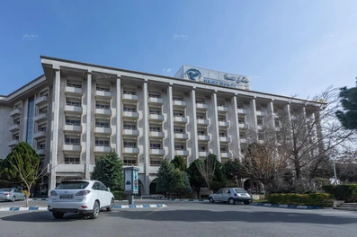 نمای ساختمان 5 طبقه هتل هما 2 مشهد با تابلو هتل هما 2 و فضای سبز جلوی ورودی هتل