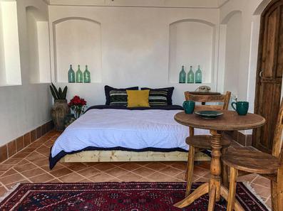 یک تخت دو نفره و ملحفه سفید و بالشت زرد در اقامتگاه سنگ پلوی کاشان