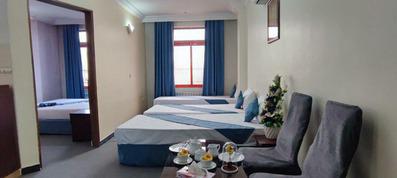 اتاق 5 تخته با سه تخت یک نفره و یک تختدو نفره در اتاق که ملحفه سفید و رو انداز آبی فیروزه ای دارند. پنجره اتاق با پرده آبی تزیین شده است.