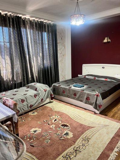 اتاق سه نفره در هتل احم نزلی که در آن یک تخت دو  نفره و تخت یک نفره با ملحفه های خاکستری براق دیده می شود