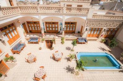 نمای بالا از یک حیاط قدیمی سنتی به سبک ایرانی با میز و صندلی در سمت چپ حیاط. پنجره های چوبی بلند در اطراف حیاط سرای سهوک کاشان به چشم میخورد.