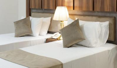 دو تخت یک نفره در هتل شایان تبریز. ملحفه سفید روی تخت ها قرار دارد. چراغ خواب کوچک و زیبا روی میز بین دو تخت قرار دارد.