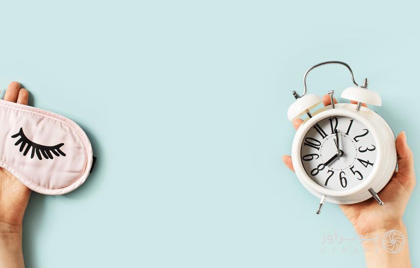 دستی در گوشهی سمت راست کادر یک ساعت رومیزی را نگه داشته و دستی در گوشهی سمت چپ کادر، یک چشمبند خواب را. جت لگ یا پرواززدگی؛ علایم و راههای درمان